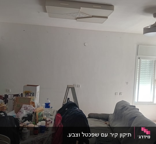 צביעת קירות בסלון דירה מרוהטת עם ספה מכוסה וסולם עבודה